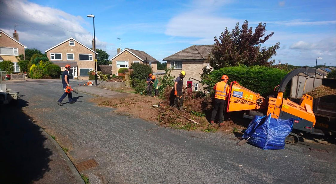 The Hocus Crocus team in hi vis feeding brash into a wood chipper on a residential street after tree work, with a tipper alongside