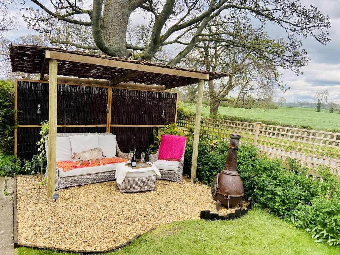 A garden with a hazel roofed pergola and seating, looking out over open fields