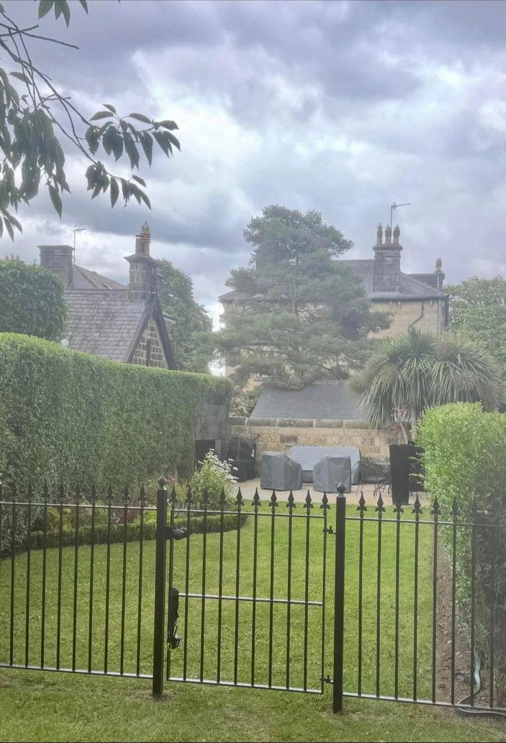 Mown lawn behind iron railings with a clipped hedge at a stone town house