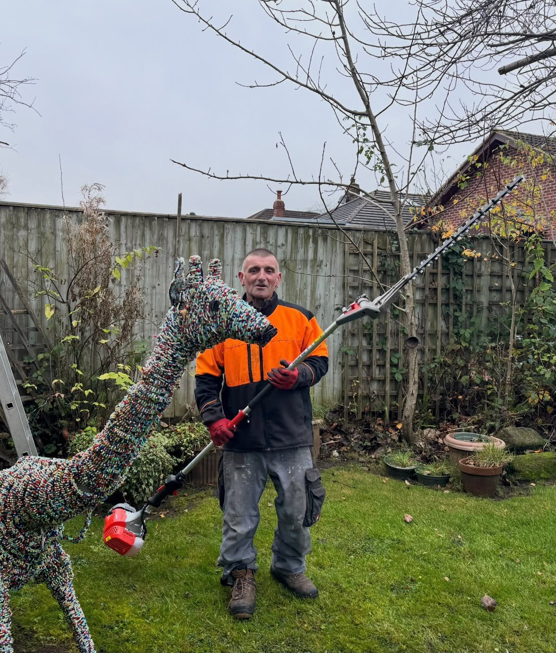 One of the team with a long reach hedge trimmer in a back garden