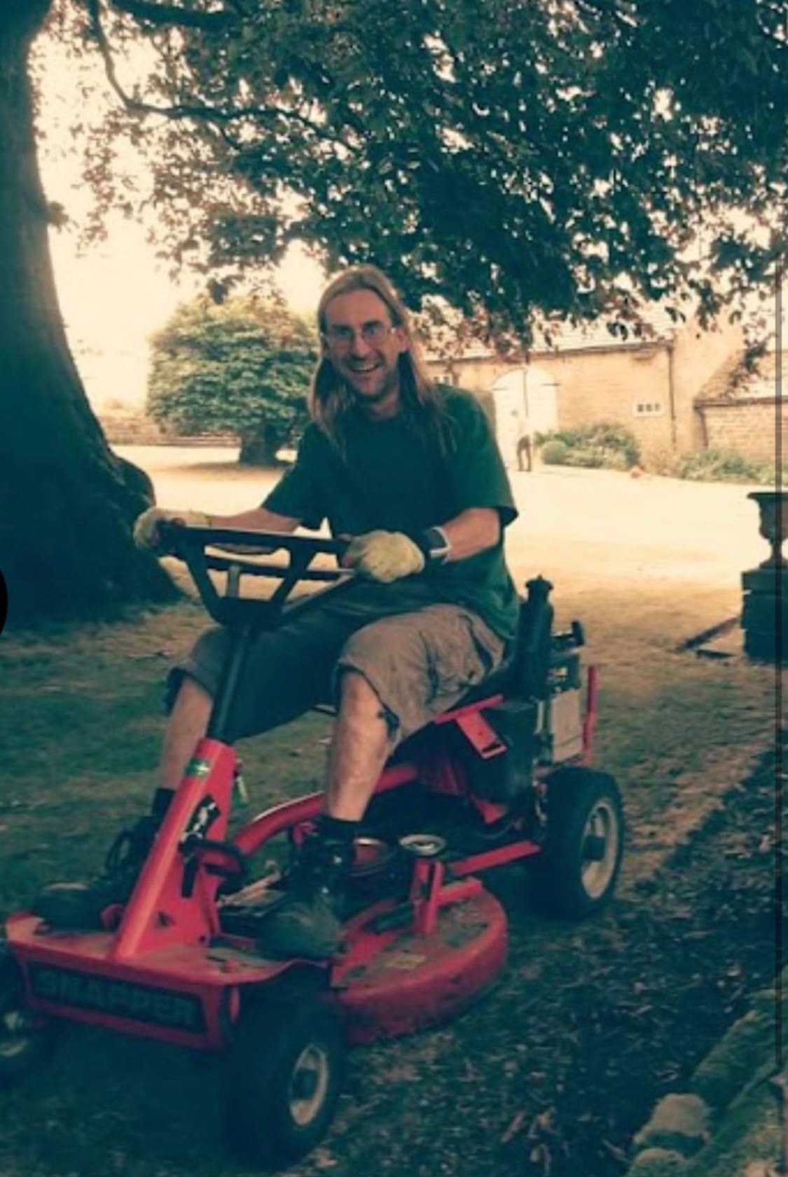 One of the team on a ride-on mower under a mature tree