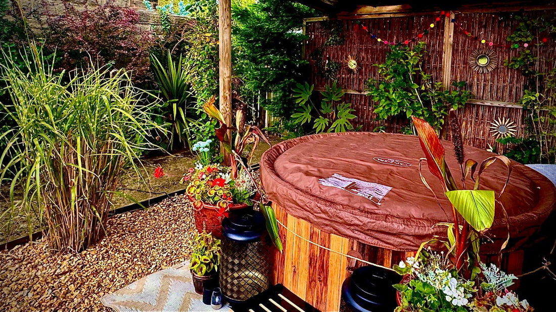 Wider view of the same barrel hot tub with a gravel bed, tall grasses and a stone wall behind