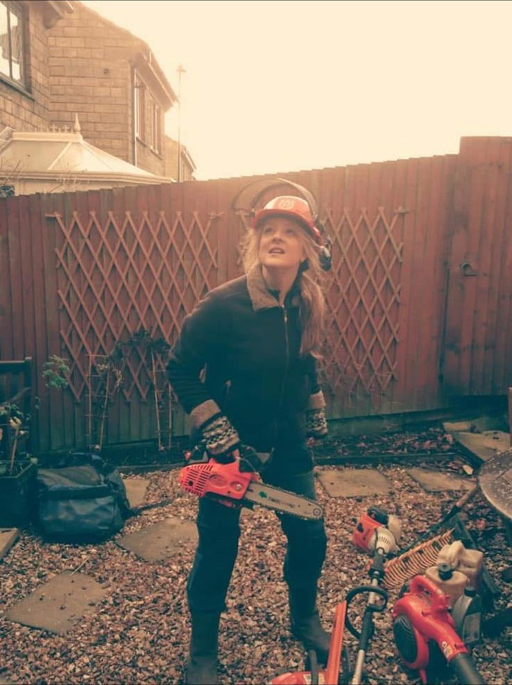 Karen in chainsaw helmet and ear defenders with her saw on a back garden tree job