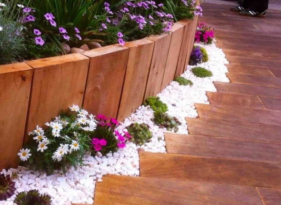 An oak sleeper raised bed planted with alpines, edged in white chippings beside hardwood decking