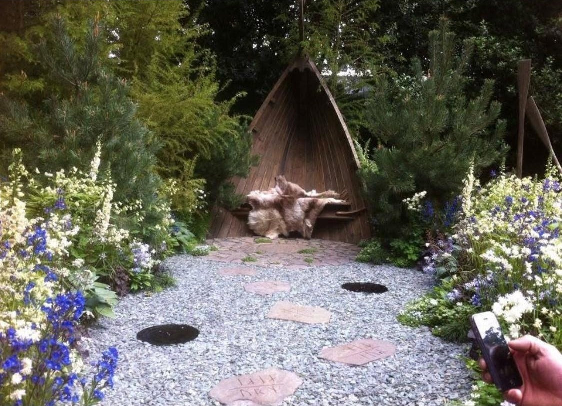 A show garden with a timber shelter, carved stepping stones and blue and white planting